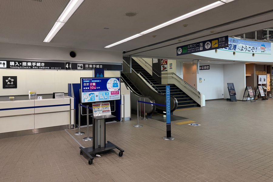 富山空港1階の入口。搭乗手続きカウンターの先に、2階へ上がるエスカレーターと階段がある