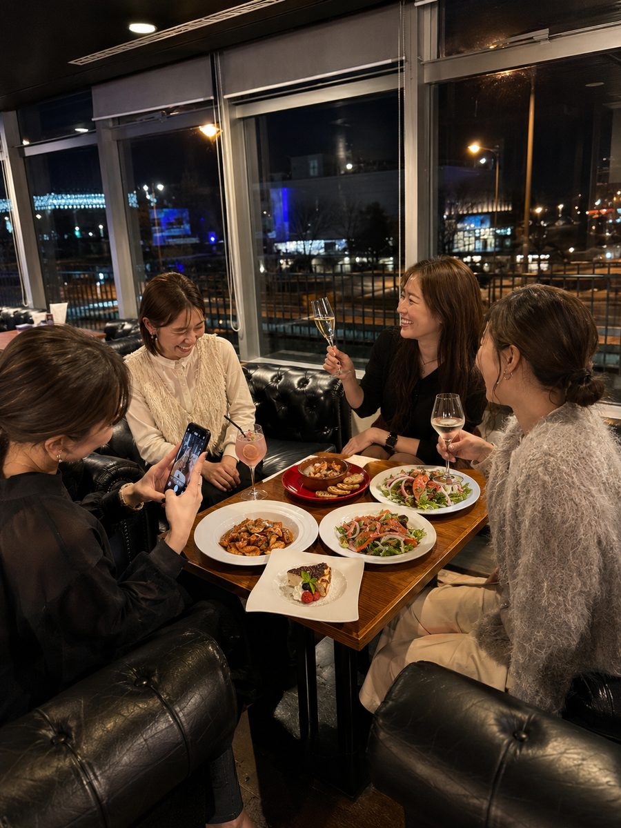 窓際の席で料理とスパークリングを囲む、友人グループの食事会